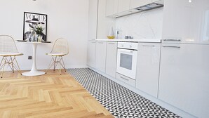 A modern kitchen with white cabinets, a white countertop, and a black and white patterned floor. There is a white table with two chairs and a gold pendant light. - Apartamenty - ul. Marszałkowska 85 (Warsaw)