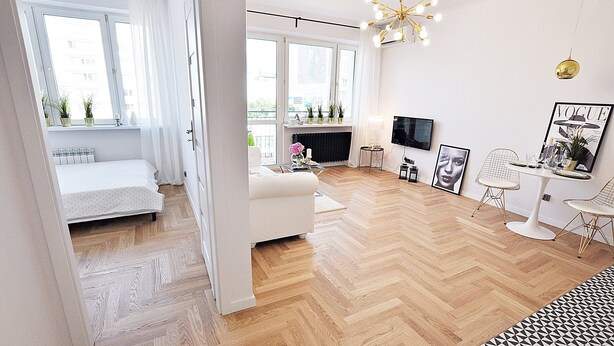 A modern living room with a sofa, a TV, and a dining area with chairs. - Apartamenty - ul. Marszałkowska 85 (Warsaw)