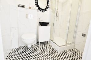 A bathroom with a white toilet, a black sink, a glass shower enclosure, and a patterned floor. - Apartamenty - ul. Marszałkowska 85 (Warsaw)