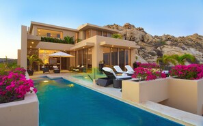 Una casa moderna con piscina, sillas de descanso y vistas a terreno rocoso.