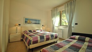 A bedroom with two beds, a nightstand, a lamp, a window with curtains, and a painting on the wall. - Residenza Venus - Venus Grazioso bilocale -50 mt dal mare (Castiglioncello)