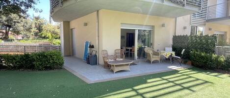 Un edificio residencial con balcón, puerta corredera de vidrio, mobiliario exterior y césped cuidado.