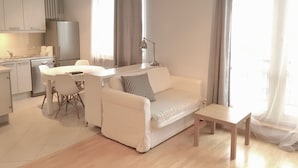A modern living room with a white sofa, a dining table with chairs, a small wooden table, and a kitchen area with a refrigerator and cabinets. - Apartament balkon-Aleje Jerozolimskie 29 (Warsaw)