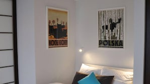 A bedroom with a bed, white bedding, and two pillows. There are two wall decorations, one with a cityscape and the other with a tree. - Apartament balkon-Aleje Jerozolimskie 29 (Warsaw)