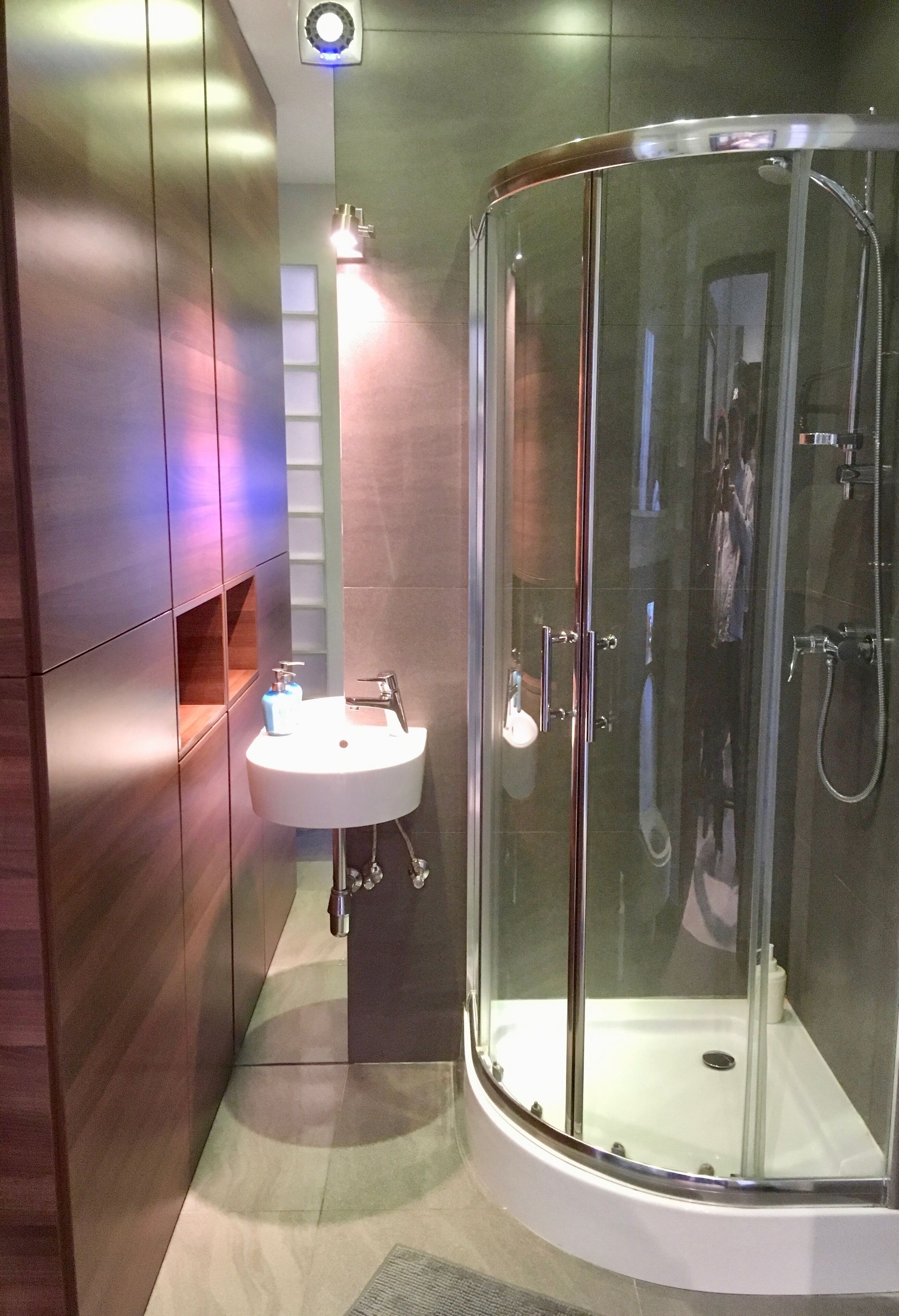 A modern bathroom with a glass-enclosed shower, a white sink, and wooden cabinetry.