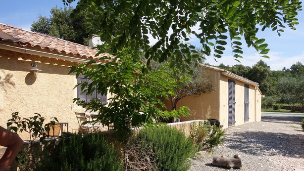 A rustic building with a tiled roof, a gravel driveway, and a black dog lying on the ground.