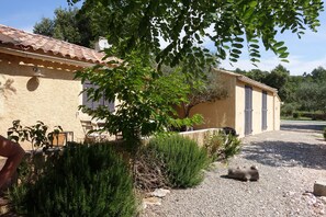 A rustic building with a tiled roof, a gravel driveway, and a black dog lying on the ground. - Charming house in an exceptional Mediterranean setting (Cotignac)