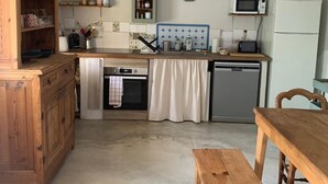A kitchen with wooden cabinets, a wooden table, a bench, a microwave, a refrigerator, and a clock on the wall.