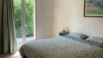 Une chambre à coucher avec un lit, une table de chevet, un tableau et une vue sur la verdure par la fenêtre.