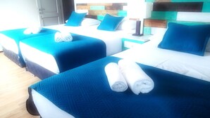 Dos camas con ropa de cama azul y almohadas blancas, un cabecero de madera y una mesita de noche pequeña con una lámpara.