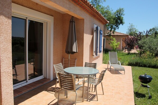 A patio with a round table and chairs, a barbecue grill, and a sliding glass door. - 2-bedroom, 5-foot air-conditioned villa with a shared heated and covered pool (Cébazan)