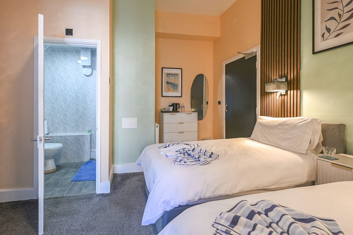 A bedroom with a bed, a bedside table, a nightstand, a mirror, and a bathroom with a toilet and shower.