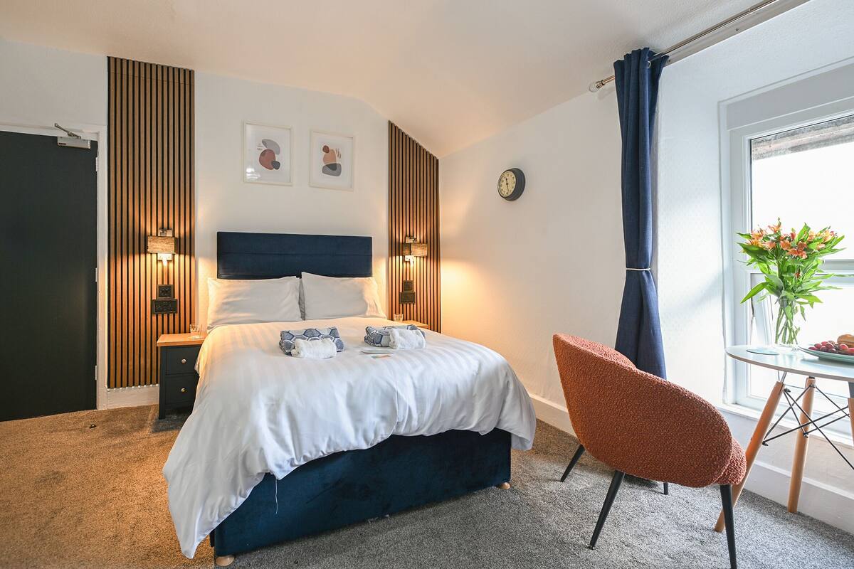 A bedroom with a bed, bedside tables, a clock, a window with curtains, and a chair.