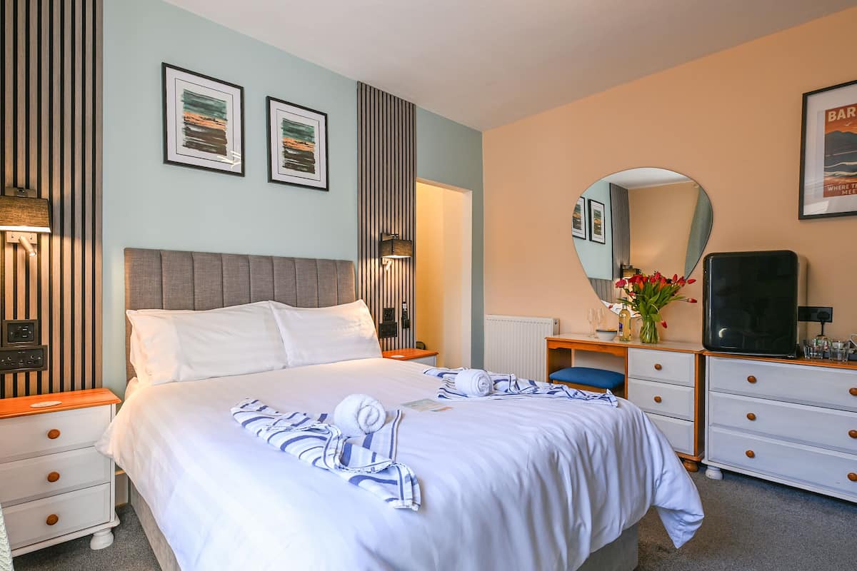 A neatly arranged hotel room with a bed, bedside tables, a dresser, a mirror, and framed artwork on the walls.