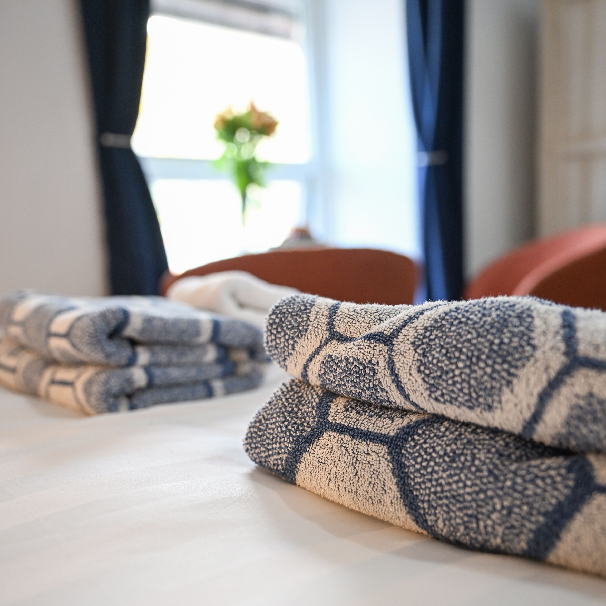 A neatly made bed with folded towels and a window with curtains in the background.
