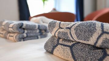 A neatly made bed with folded towels and a window with curtains in the background.