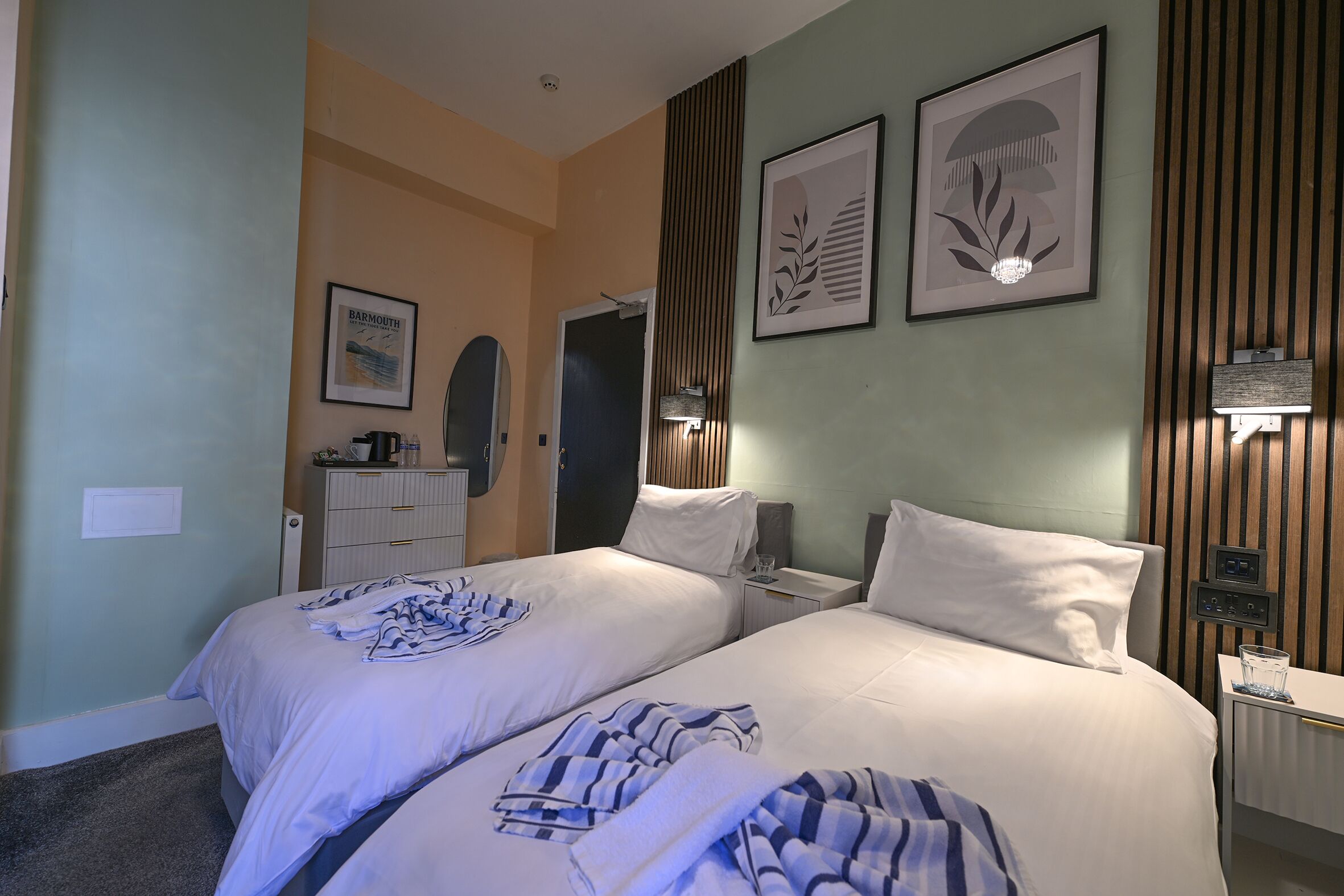 A hotel room with two beds, a dresser, a mirror, and framed artwork on the walls.