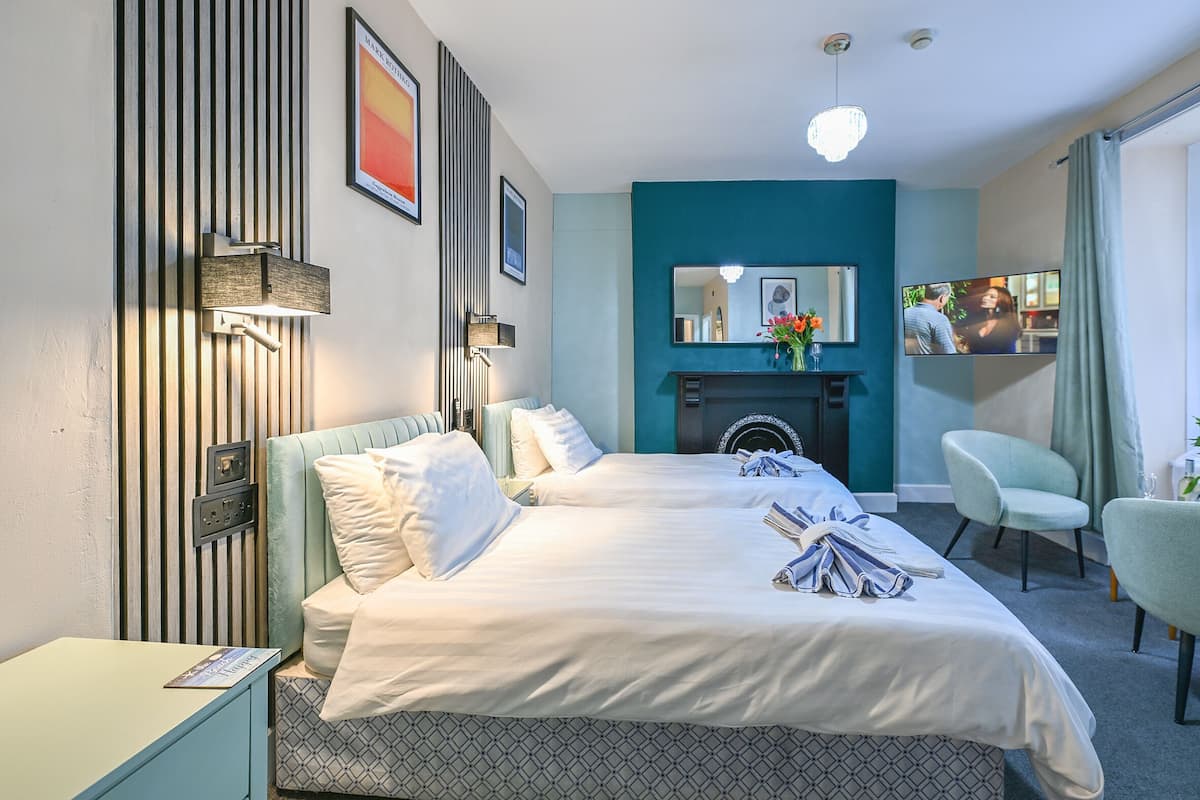 A hotel room with a bed, a desk, a chair, a TV, and a fireplace.