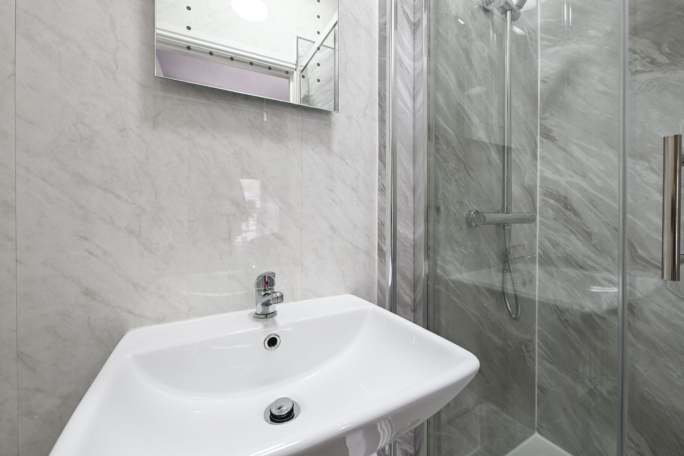 A bathroom with a white sink, a mirror, and a glass shower enclosure.