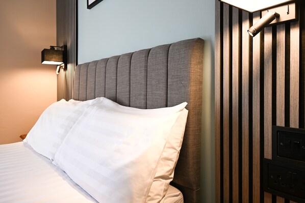 A neatly made bed with white linens, a padded headboard, and a wall-mounted light fixture.