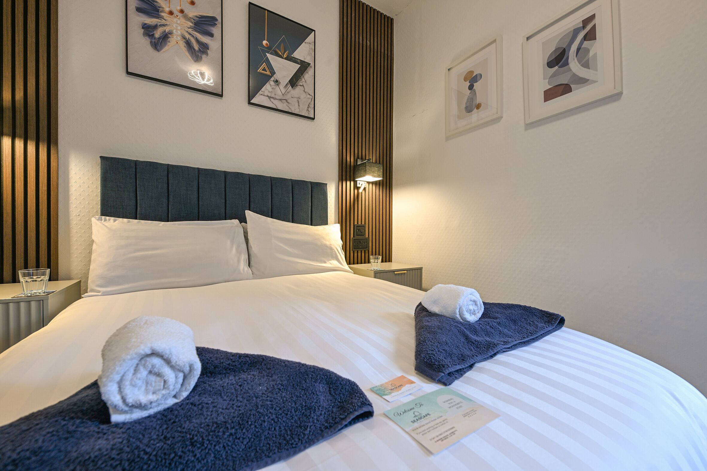 Una cama bien hecha con toallas, un cabecero y una obra de arte enmarcada en la pared.