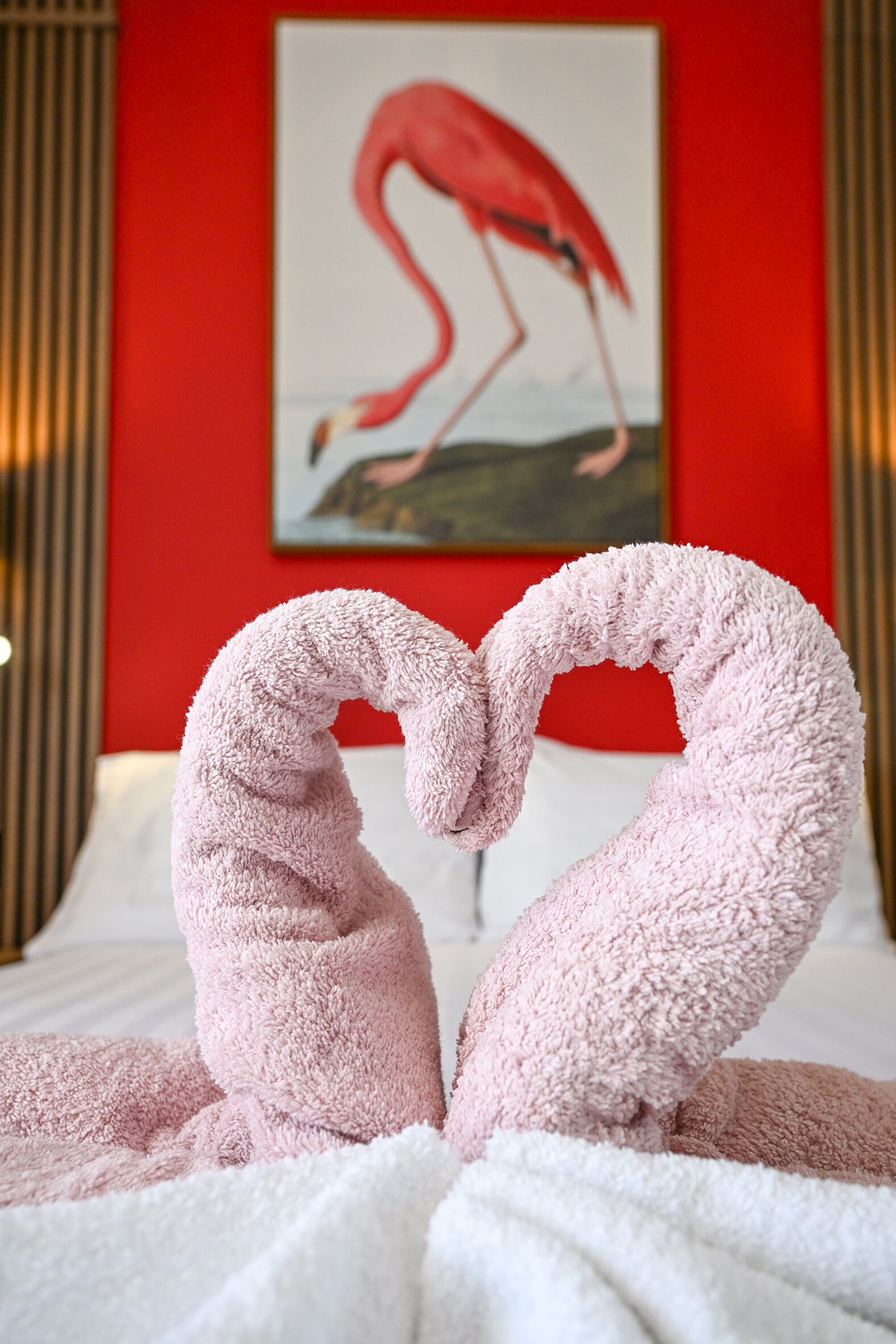 Una cama con sábana blanca y un corazón hecho con una toalla rosa.