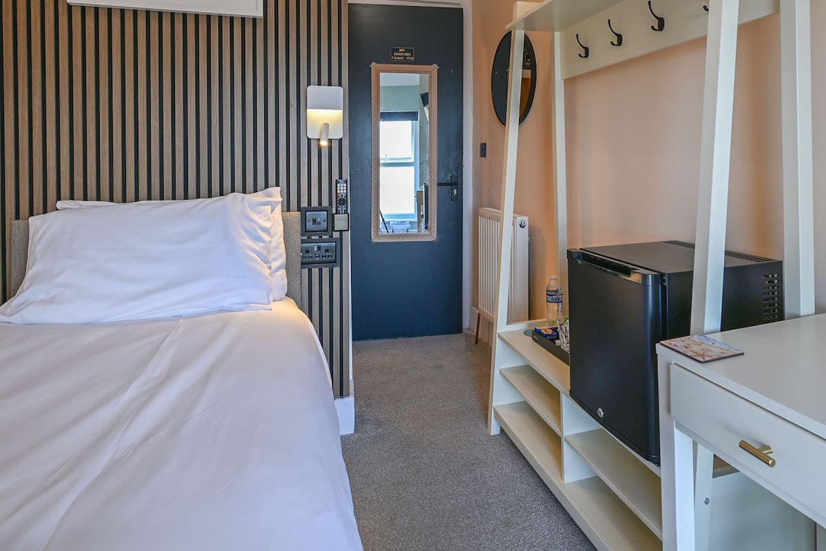 A hotel room with a bed, a desk with a TV, a mirror, a clock, and a butterfly artwork on the wall.