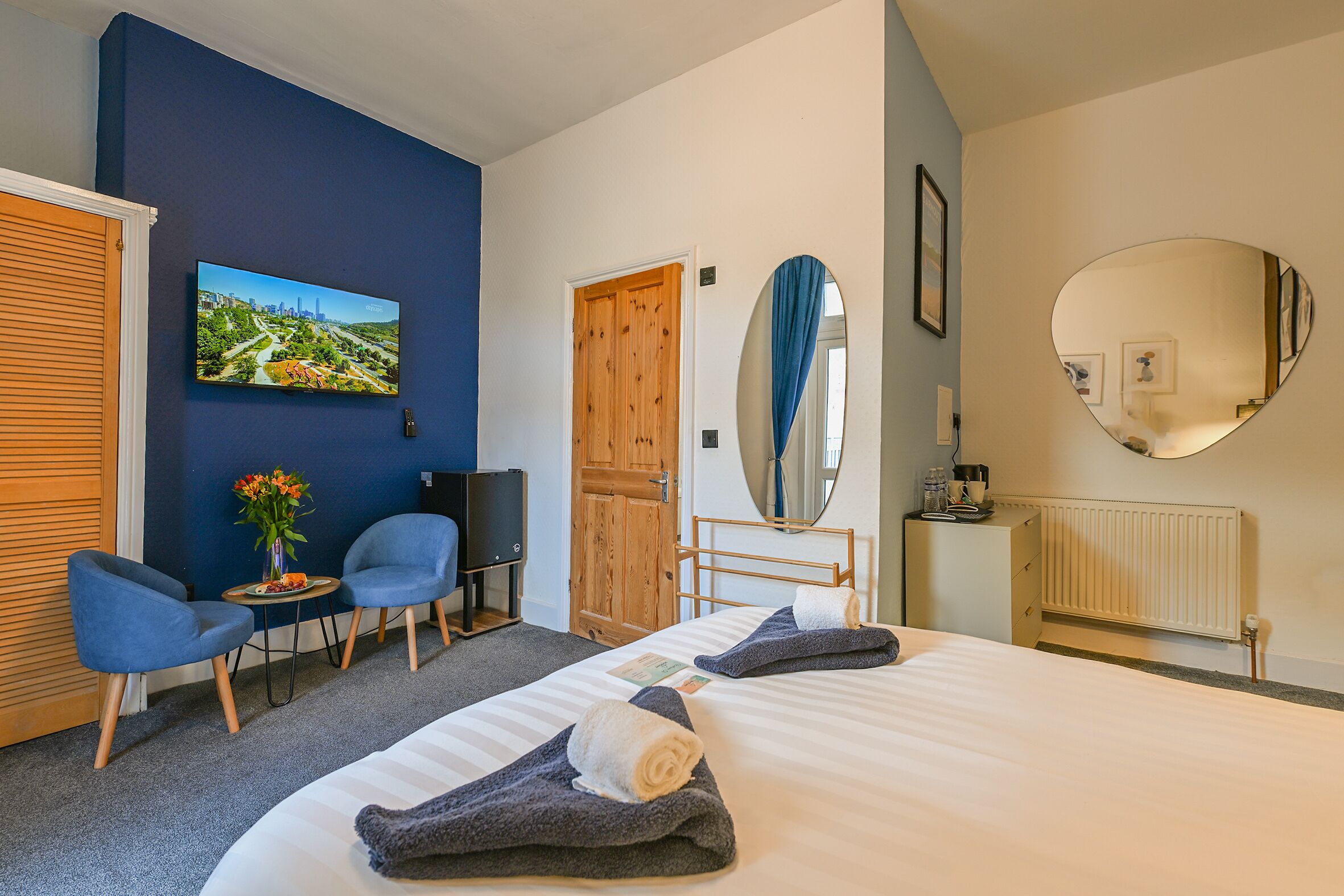 A hotel room with a bed, two chairs, a TV, a wooden door, a mirror, and a radiator.