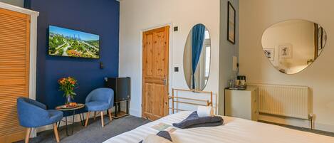 A hotel room with a bed, two chairs, a TV, a wooden door, a mirror, and a radiator.