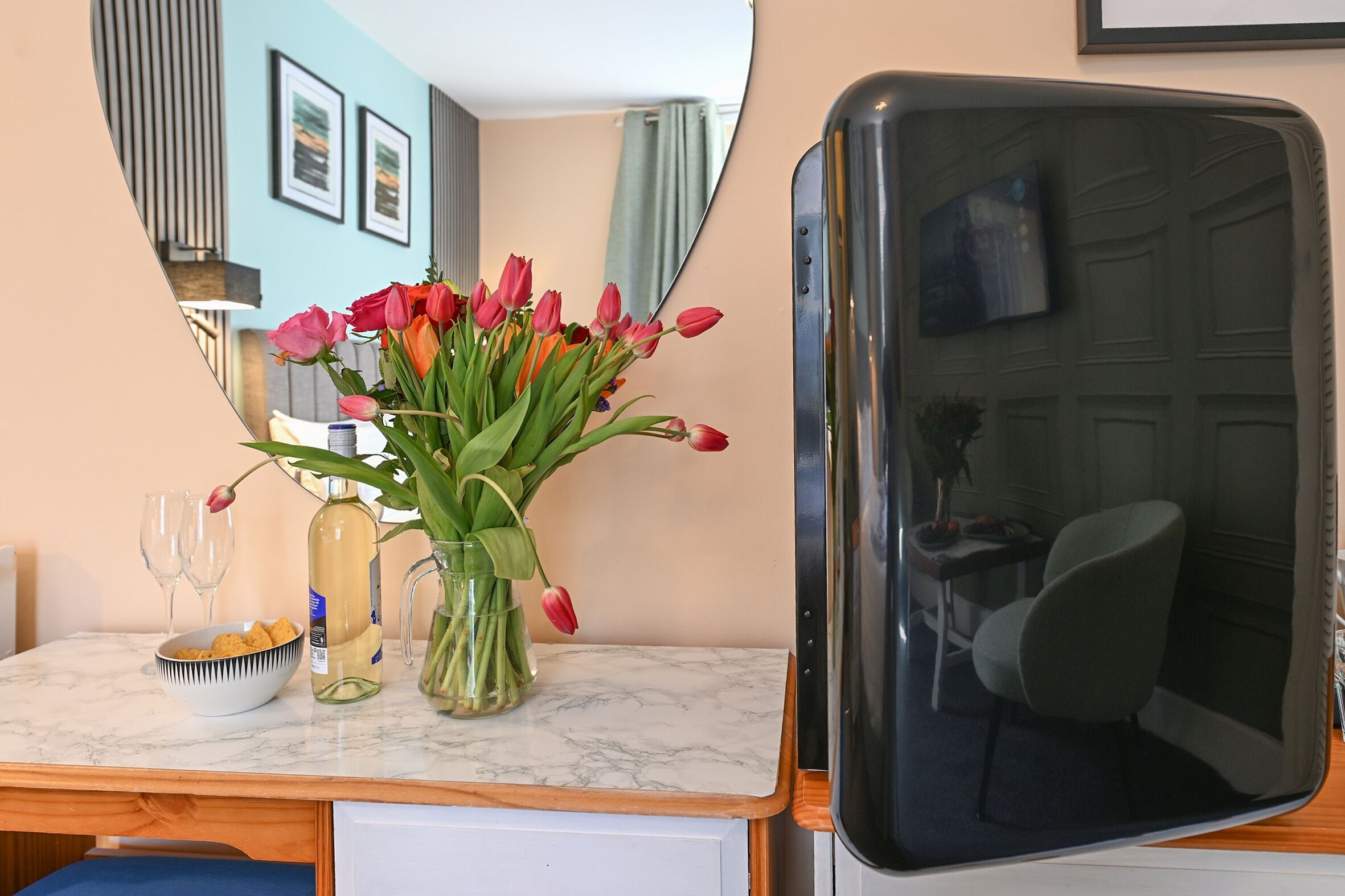 A room with a marble countertop, a vase with flowers, a bowl of snacks, and a television.