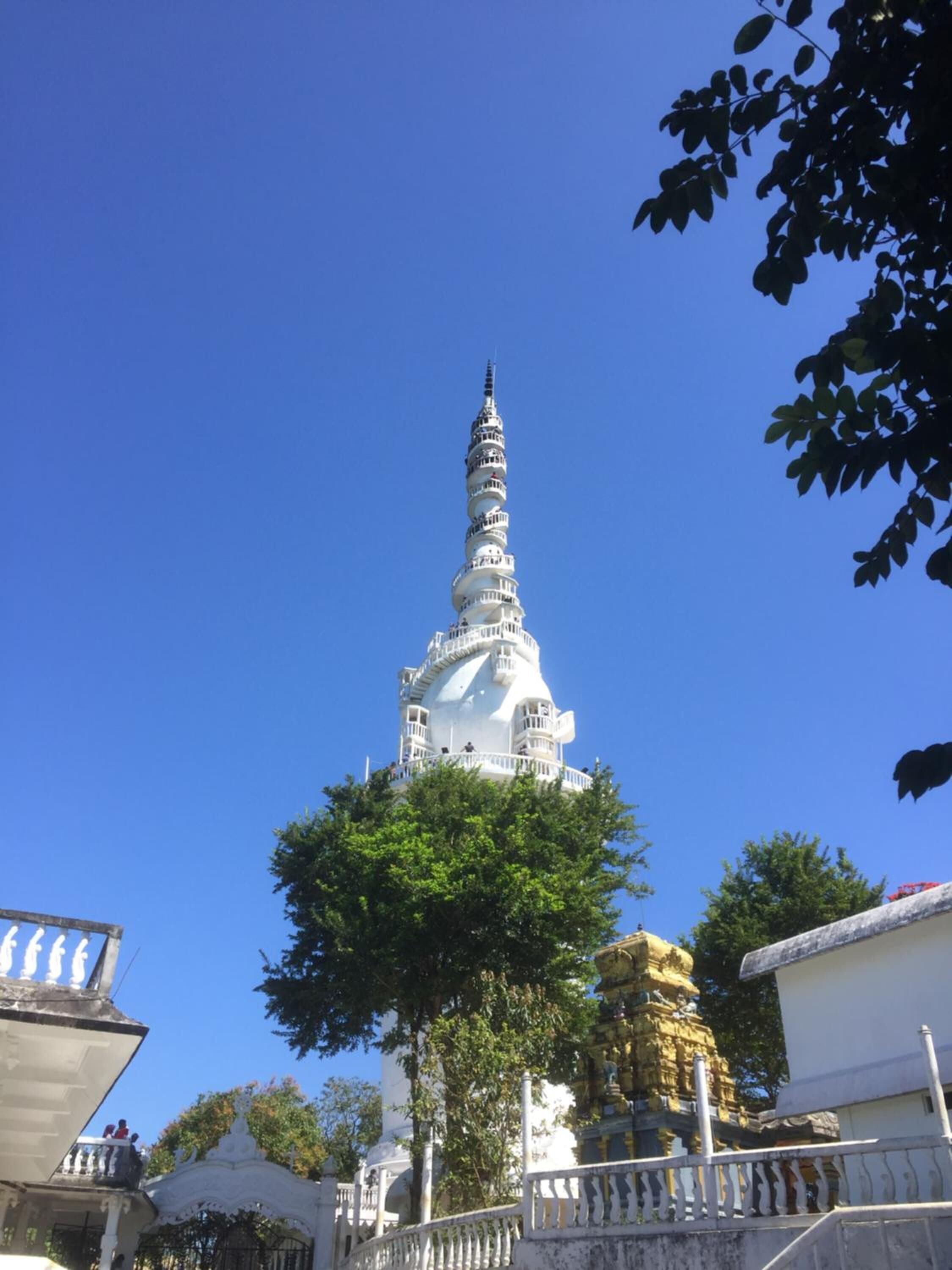 A white pagoda-like structure with a spiral design, surrounded by greenery and a white fence.