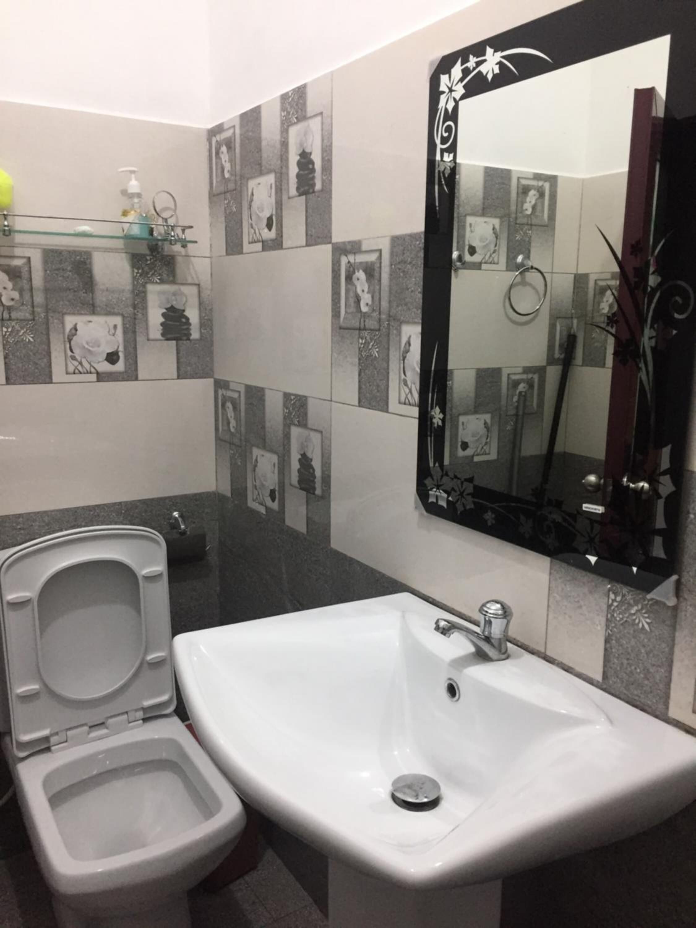 A bathroom with a toilet, sink, and mirror. The walls have a checkered tile pattern with framed pictures.