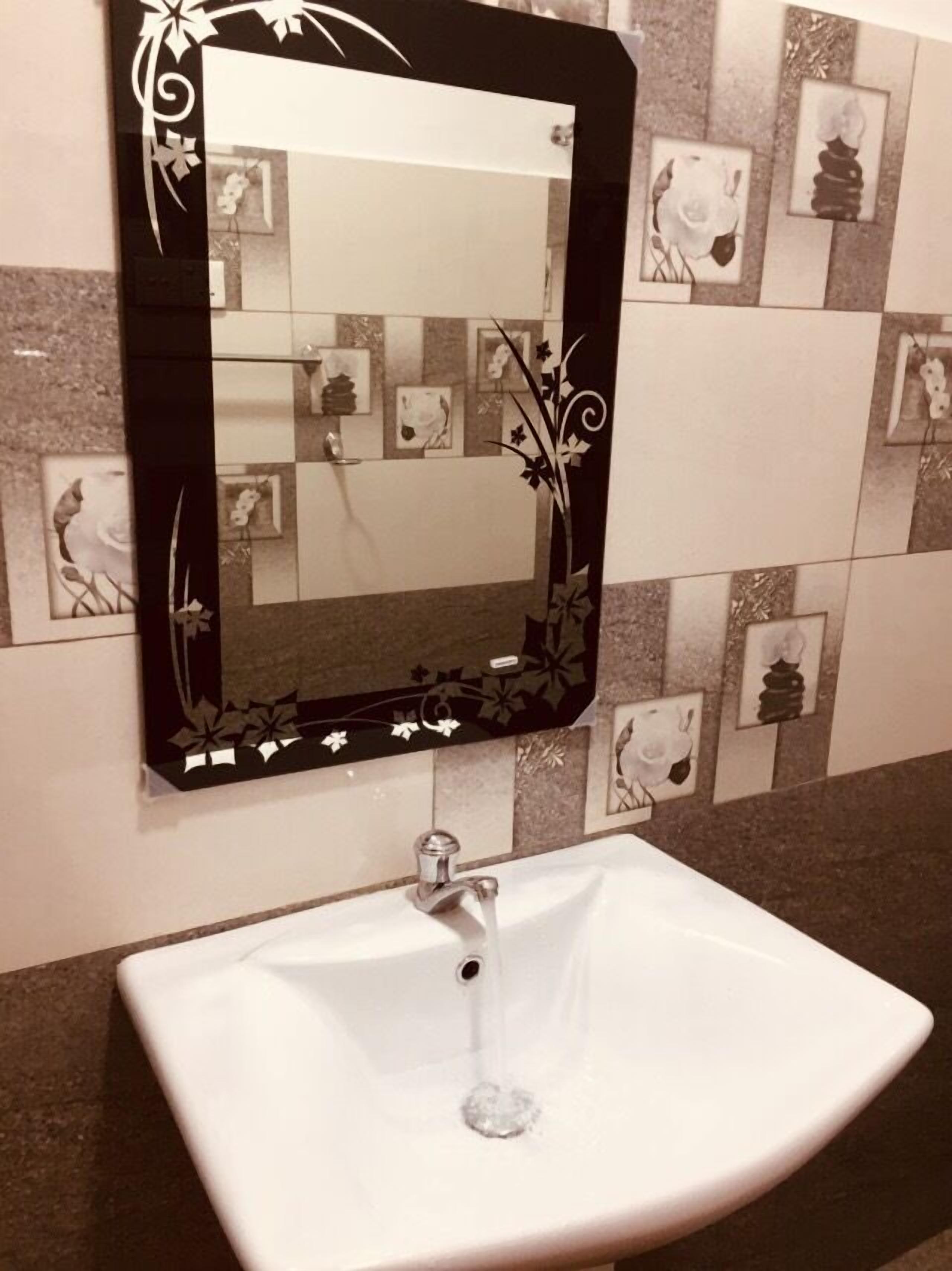 Une salle de bain avec un lavabo blanc, un miroir à cadre noir et des carreaux décoratifs.