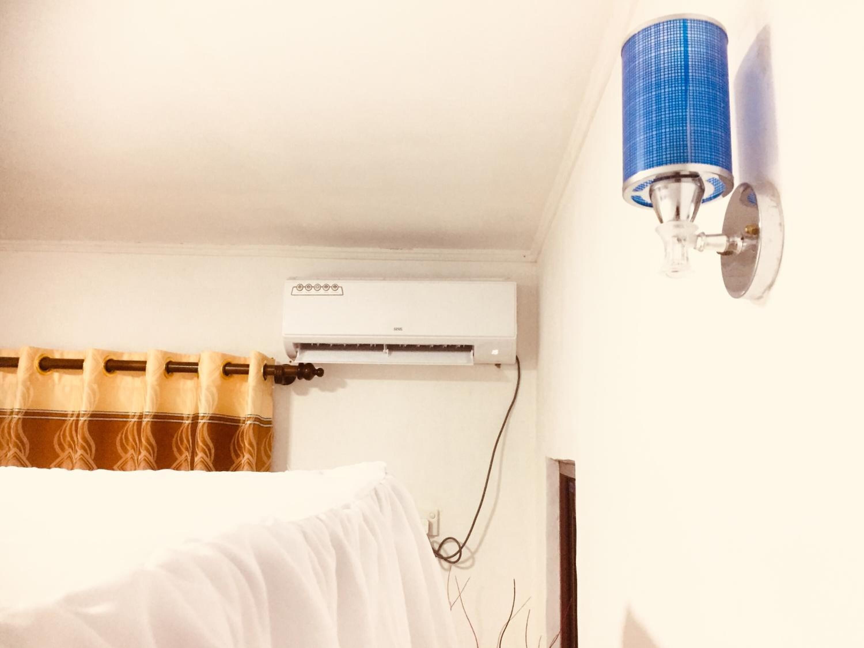 A room with a white air conditioner mounted on the wall, a blue cylindrical object on the wall, and a curtain with a brown and beige pattern.