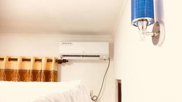 A room with a white air conditioner mounted on the wall, a blue cylindrical object on the wall, and a curtain with a brown and beige pattern.