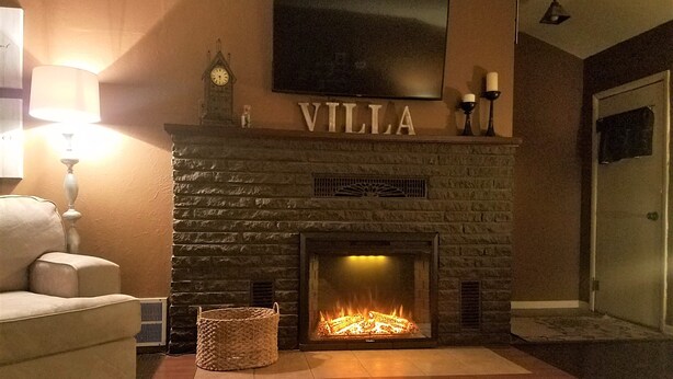 En murstenspejs med et TV ophængt over, et ur og ordet 'VILLA' på væggen.