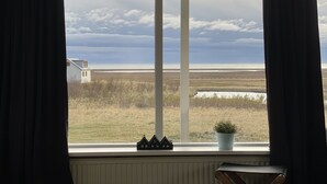 Una habitación con un ventanal grande que da a un paisaje costero, con un modelo de casa y una planta en maceta en el alféizar.