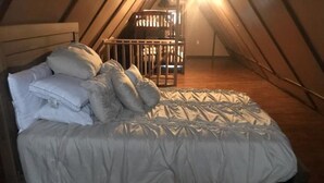 Un dormitorio con cama, almohadas y cuna en una habitación con techo inclinado.