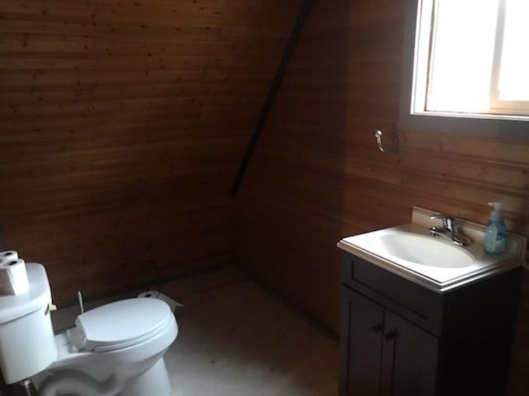 Ein kleines Badezimmer mit Holzwandverkleidung, Toilette, Waschbecken und Fenster.