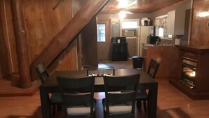 Un comedor con una mesa y sillas de madera, una escalera y una cocina al fondo.