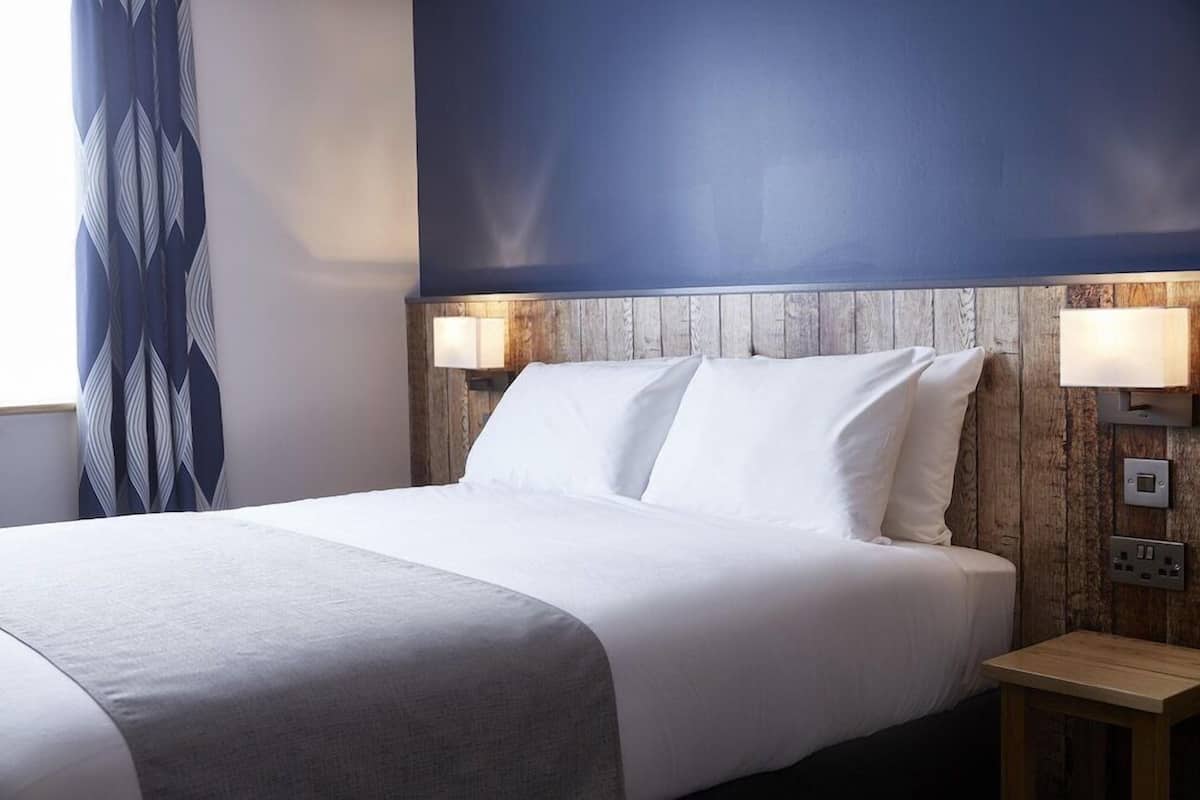 A hotel room with a bed, two bedside lamps, a wooden headboard, and a nightstand.