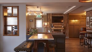 A cozy bar area with a wooden bar counter, cushioned stools, and pendant lighting. - The Churchill By Greene King Inns (Swindon)