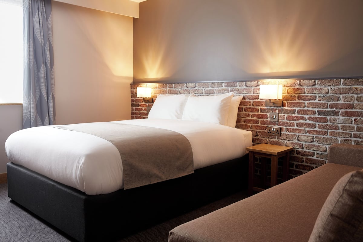 A hotel room with a large bed, a small bedside table, and a brick-patterned headboard.