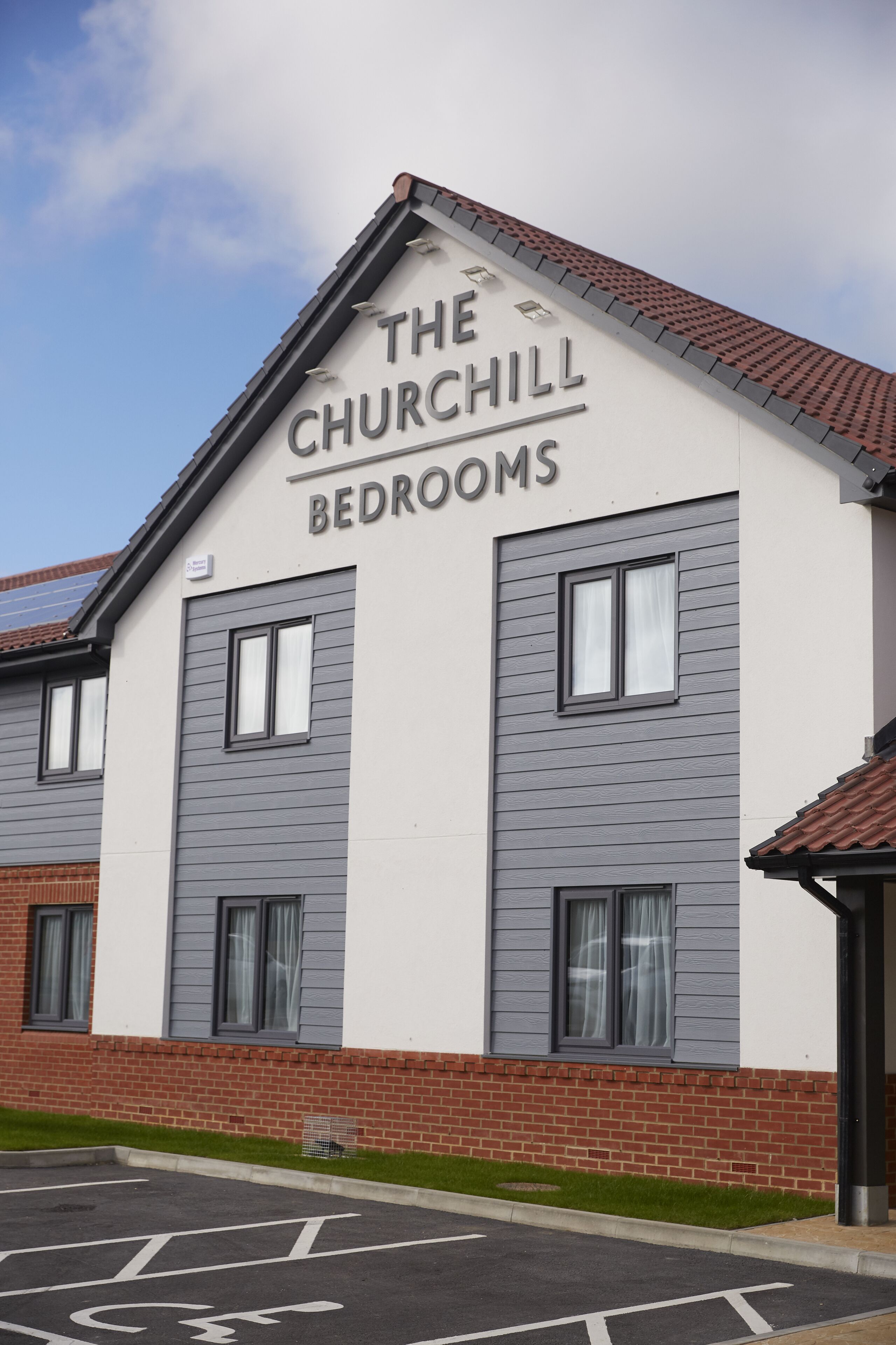 A building named "The Churchill Bedrooms" with a modern architectural design, featuring a brick base and grey siding.