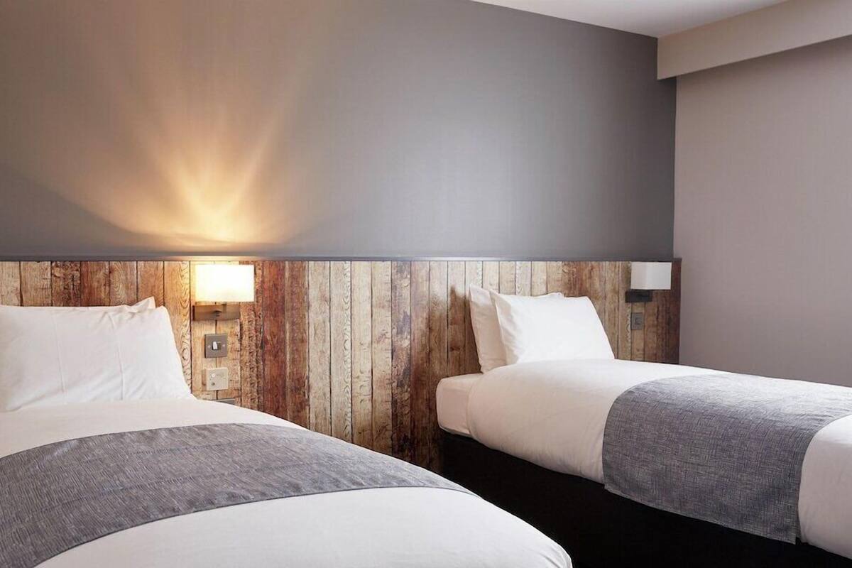 A hotel room with two beds, a wooden headboard, and a wall-mounted light fixture.