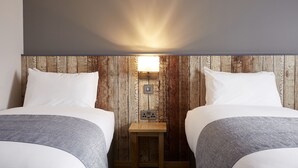 A room with two beds, a wooden wall, a small table with a lamp, and a power outlet. - The Churchill By Greene King Inns (Swindon)