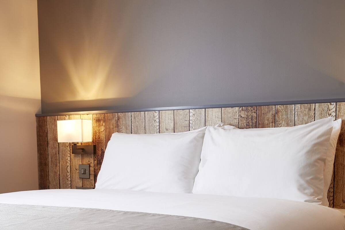 A neatly made bed with white linens and a wooden headboard.