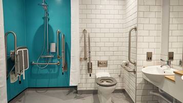 Et moderne badeværelse med blå vægdetaljer, et hvidt toilet, en vask og en brusekabine med gelænder.