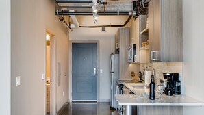 A modern kitchen with stainless steel appliances, a white countertop, and wooden bar stools. - MINNeSTAY* Sable 803 | North Loop | Target Center (Minneapolis)