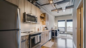 A modern kitchen with stainless steel appliances, wooden cabinets, and a large window offering a city view. - MINNeSTAY* Sable 803 | North Loop | Target Center (Minneapolis)
